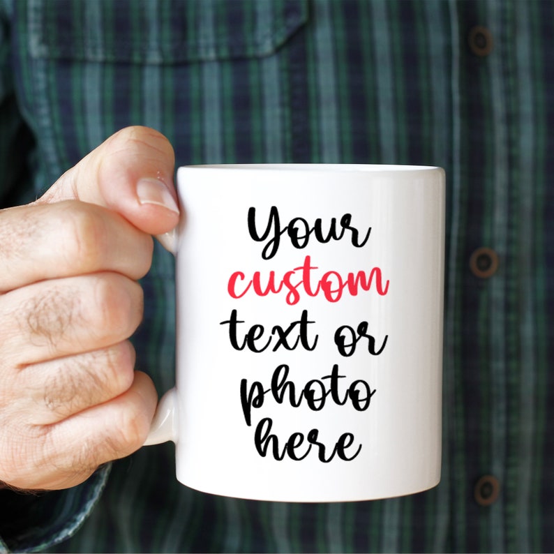 May include: White ceramic mug with a black handle. The mug has black text that says "Your custom text or photo here" with the word "custom" in red.