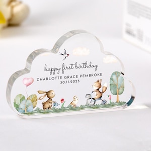May include: A clear acrylic cloud-shaped keepsake with a watercolor illustration of a bunny, fox, and bird in a forest setting. The text "happy first birthday CHARLOTTE GRACE PEMBROKE 30.11.2025" is printed on the cloud.