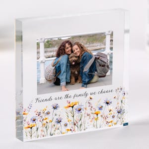 Könnte beinhalten: Ein klarer Acryl-Fotoblock mit einem Foto von zwei Personen und einem Hund. Der Boden des Blocks ist mit einem Aquarell-Blumenmuster in Gelb-, Blau- und Lilatönen verziert. Der Text "Friends are the family we choose" ist auf dem Block aufgedruckt.