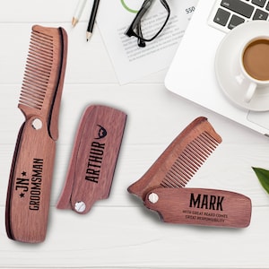 Könnte beinhalten: Drei Holz-Taschenkamm mit personalisierten Gravuren. Die Kämme sind braun und haben ein Klappdesign. Die Gravuren beinhalten die Namen "JN* GROOMSMAN", "ARTHUR" und "MARK WITH GREAT BEARD COMES GREAT RESPONSIBILITY".