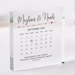 Puede incluir: Un bloque de acrílico transparente con un calendario para septiembre de 2025, con la fecha 10 marcada. El texto "Meghan & Noah" está en la parte superior del calendario, y el texto "¡Felicidades por su boda! ¡Les deseamos una vida llena de felicidad juntos! 10/09/25" está en la parte inferior.