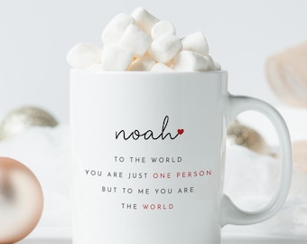 May include: White ceramic mug with a black inscription that reads "noaho" with a small red heart. The text below reads "To the world you are just one person but to me you are the world".