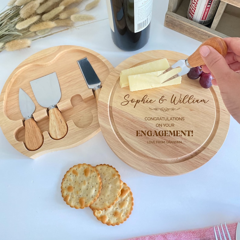 May include: A wooden cheese board with a round serving area and a separate compartment for cheese knives. The board is engraved with the text "Sophie & William Congratulations on your Engagement! Love from Grandma".