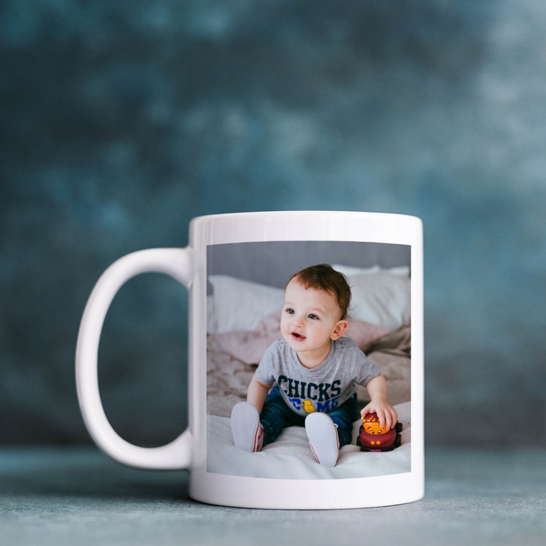 May include: White ceramic mug with a photo of a baby boy sitting on a bed, wearing a gray shirt with the text "CHICKS TO ME" printed on it. The baby is holding a red toy.