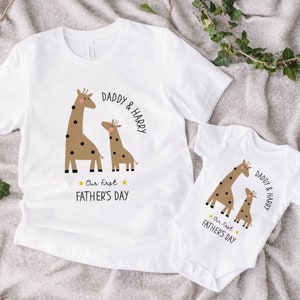 May include: Two white t-shirts with a giraffe design and the text "Daddy & Harry" and "Our First Father's Day".