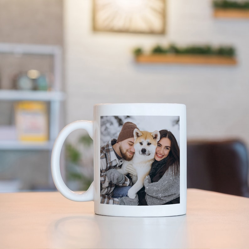 May include: White ceramic mug with a photo of a couple and their dog in a snowy setting. The couple is wearing winter clothing and the dog is a brown and white Akita.
