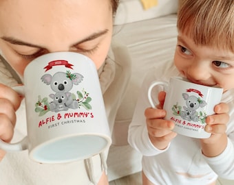Könnte beinhalten: Weiße Keramikbecher mit einem Koala-Bären-Design und dem Text "ALFIE & MUMMY'S FIRST CHRISTMAS". Das Design umfasst einen Koala-Bären mit einem Baby-Koala, Stechpalme und ein rotes Banner mit dem Jahr 2025.