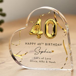 May include: A clear heart-shaped acrylic paperweight with gold foil confetti and gold balloon numbers "40" inside. The text "Happy 40th Birthday Sophie Lots of Love Olivia, Alfie & Noah" is printed on the paperweight.