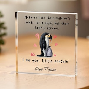 May include: A clear acrylic block with a quote about mothers and children, featuring a penguin and a baby penguin. The quote reads "Mothers hold their children's hands for a while, but their hearts forever." The block also includes the text "I am your little penguin" and "Love Megan".