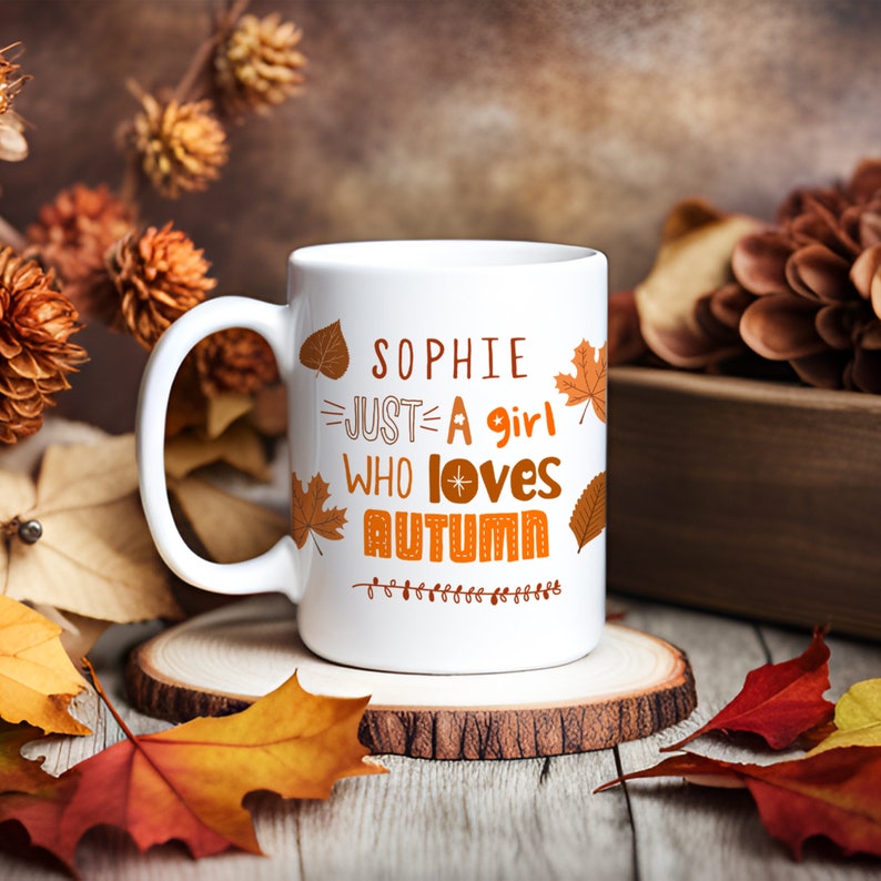 May include: White ceramic mug with a brown and orange design. The mug says "Sophie Just A Girl Who Loves Autumn" with a star and leaves.