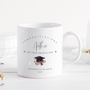May include: White ceramic mug with a graduation theme. The mug features the text "Congratulations Arthur on your graduation" and the University of Bath, 2024. A graduation cap and diploma are also illustrated.