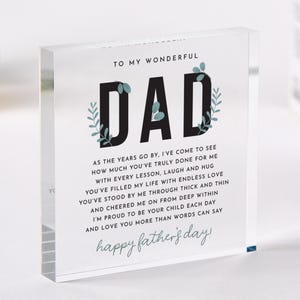 May include: A clear acrylic block with the word "DAD" in large black letters, decorated with teal leaf accents. The block features a heartfelt message for Father's Day, with the words "happy father's day!" at the bottom.