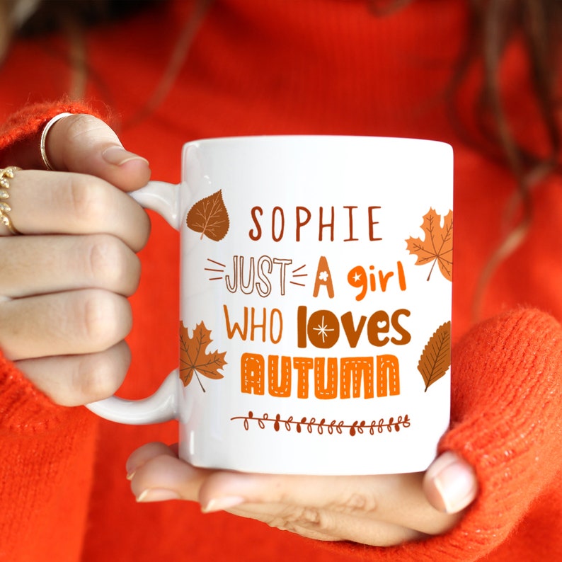 May include: White ceramic mug with a brown and orange autumn leaf design. The mug has the text "Sophie Just A Girl Who Loves Autumn" with a star design.