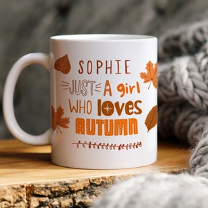 May include: White ceramic mug with a brown and orange autumn-themed design. The mug reads "Sophie Just A Girl Who Loves Autumn" with a small star and a stitched autumn word.