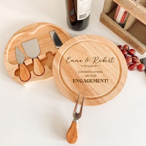 May include: Wooden cheese board with a removable section that holds three cheese knives. The board is engraved with the text "Emma & Robert Congratulations on your Engagement!"