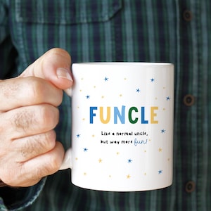 Puede incluir: Taza de cerámica blanca con la palabra "FUNCLE" en azul, amarillo y verde, con el texto "Like a normal uncle, but way more fun!" y detalles de estrellas. La taza es sostenida por una persona.
