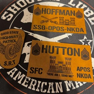 May include: Three tan leather patches with black lettering. Two rectangular patches read "HOFFMAN" and "HUTTON" with military insignia and unit designations. A third patch is shield-shaped, with "OHIO STATE HIGHWAY PATROL" and "S.R.T."
