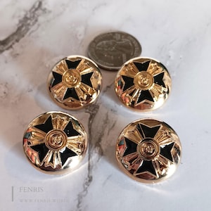 May include: Four circular gold-tone buttons featuring a black cross design with a central circular emblem. A United States quarter coin is placed near the buttons for scale, showing the relative size of the metallic hardware components.