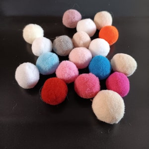 May include: A collection of colorful pom poms in various shades of pink, red, blue, white, and gray. The pom poms are arranged in a star shape on a black background.