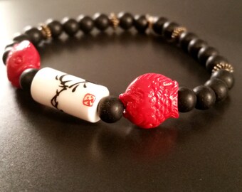 May include: A black beaded bracelet with red fish charms and a white ceramic bead with black calligraphy and a red seal.