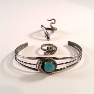 May include: A set of three silver rings with turquoise stones. The rings are all different styles, one is a snake, one is a flower, and one is a simple band with a turquoise stone.
