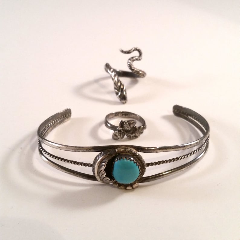May include: A set of three silver rings with turquoise stones. The rings are all different styles, one is a snake, one is a flower, and one is a simple band with a turquoise stone.