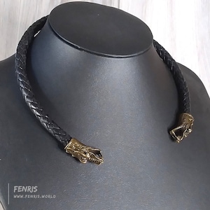 May include: A black leather choker necklace with two gold dragon head clasps. The necklace is braided and has a simple design.