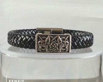 May include: Black leather bracelet with a silver metal clasp featuring a Celtic knot design with two wolves.