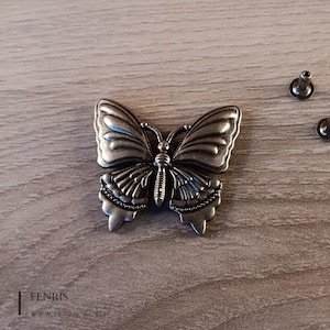 May include: A silver metal butterfly charm with intricate details. The charm has a textured surface and a delicate design.