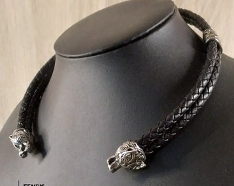 May include: A black leather choker necklace with braided design, featuring silver-colored wolf head terminals. The necklace is displayed on a black mannequin. The text "FENRIS" and website address are visible at the bottom.