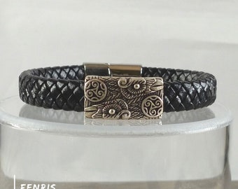 May include: A black braided leather bracelet featuring a rectangular silver-toned metal centerpiece with engraved bird motifs and triskelion symbols. The text FENRIS and WWW.FENRIS.WORLD is printed in white in the lower left corner of the image.
