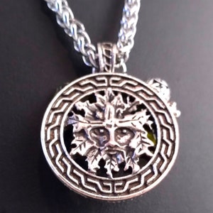 May include: Silver pendant necklace featuring a green man face surrounded by leaves, set within a circular frame with a geometric design.