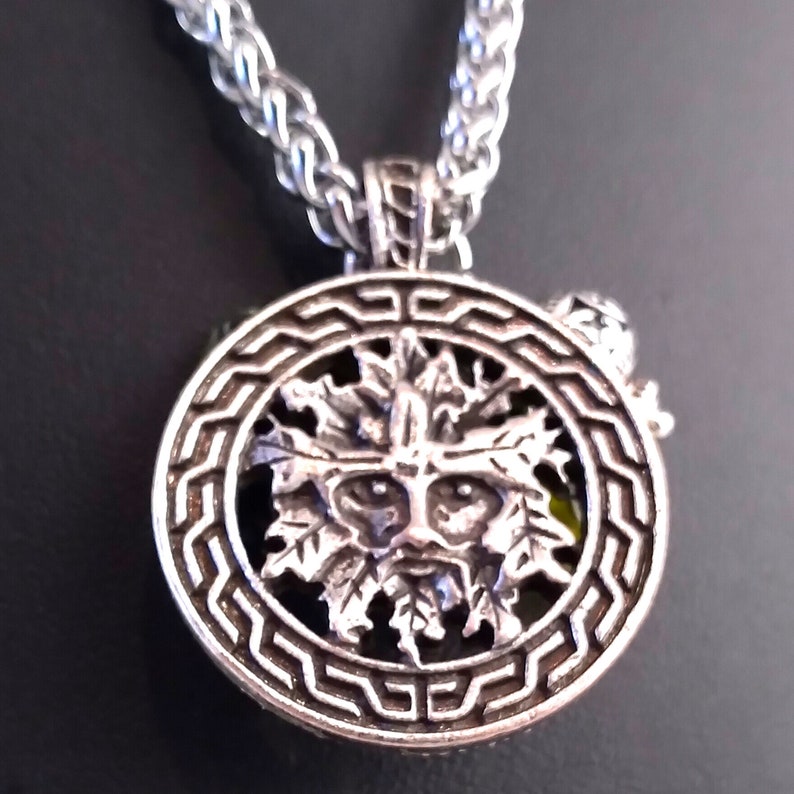 May include: Silver pendant necklace featuring a green man face surrounded by leaves, set within a circular frame with a geometric design.
