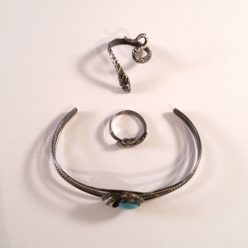 May include: Three silver rings, one with a turquoise stone, one with a snake design, and one plain band.