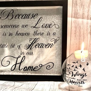 May include: A framed black and white print with the text "Because someone we love is in heaven there is a little bit of heaven in our home."  The frame is sitting on a table next to a clear glass globe with the text "Your wings were ready but our hearts were not" and a small candle inside.