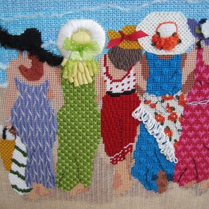 May include: Needlepoint artwork depicting five figures in dresses and hats, strolling on a beach. The figures are rendered in various colors, including blue, green, red, and pink. The background features a blue sky and sandy beach.