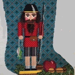 Puede incluir: Una media de Navidad con un cascanueces que sostiene una caña de pescar y un pez. La media está decorada con un patrón de rombos azul y blanco y una guirnalda verde con manzanas rojas y adornos.