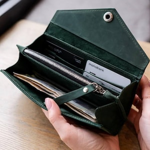 May include: A dark green envelope-style wallet with a silver snap button closure. The interior features a zippered compartment with a matching green leather pull tab, multiple card slots containing a monobank card, and a section for paper currency.