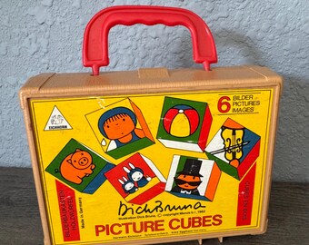 May include: A vintage toy picture cube set in a tan carrying case with a red handle. The front features colorful illustrations of cartoon characters and the text "Dich Bruna PICTURE CUBES". The set includes six picture cubes.