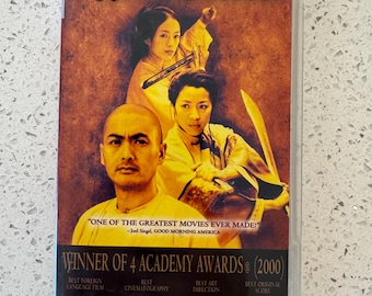 May include: A UMD Video for PSP case featuring the movie Crouching Tiger Hidden Dragon. The cover displays three actors in a warm-toned scene with text including "Winner of 4 Academy Awards (2000)" and "One of the greatest movies ever made!"