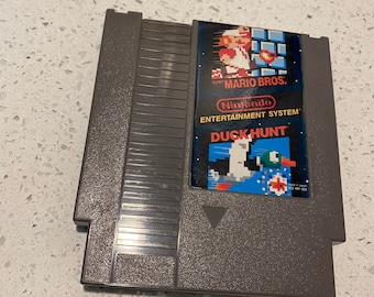 May include: A gray Nintendo Entertainment System game cartridge with a label featuring the text "Super Mario Bros." and "Duck Hunt". The label also includes a pixelated image of Mario and a duck.