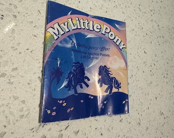 May include: A vintage My Little Pony promotional booklet. The cover features the text "My Little Pony" in a rainbow arc, with the words "Exclusive pony offer! Sensational Sparkle Ponies just for you!" The background is blue with pony silhouettes.
