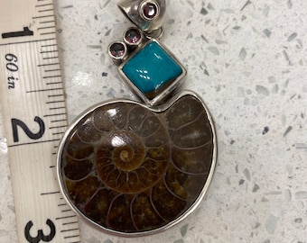 May include: A silver pendant featuring a brown ammonite fossil with a turquoise gemstone and pink accents.