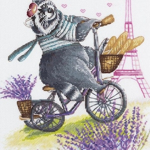 Puede incluir: Diseño de punto de cruz de un mapache en bicicleta, con baguettes y lavanda. El mapache lleva una camisa a rayas y una bufanda. La Torre Eiffel está al fondo, con corazones flotando. La bicicleta es morada.