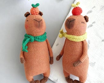 Capivara de crochê de pelúcia com laranja e cachecol, braços articulados em amigurumi.