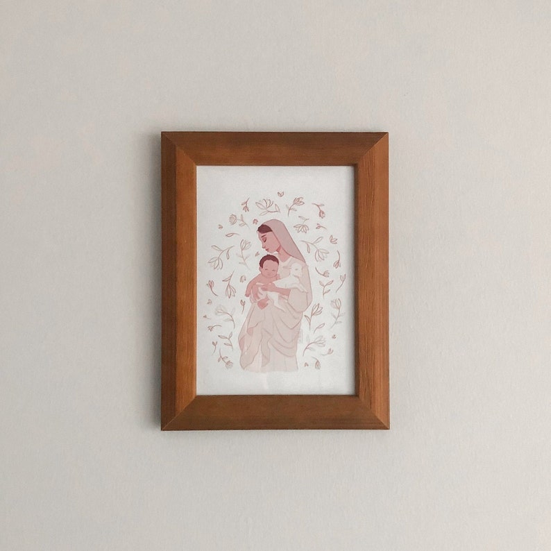 May include: A framed illustration of a woman holding a baby in her arms. The woman is wearing a white dress and a veil. The baby is wrapped in a white blanket. The illustration is surrounded by a circle of delicate flowers.
