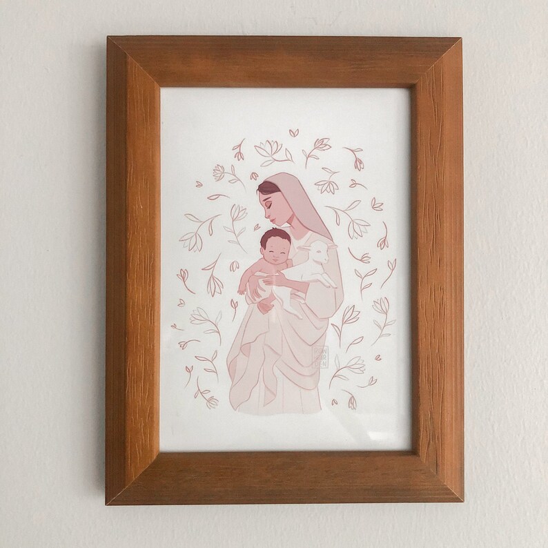 May include: A framed illustration of a woman holding a baby and a lamb. The woman is wearing a white robe and has a halo. The baby is wrapped in a white blanket. The lamb is white and has a pink nose. The background is a light pink with white flowers.