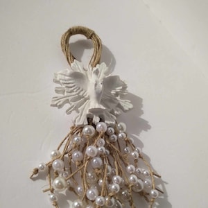Peut inclure: Une décoration en céramique blanche en forme de colombe avec une boucle en toile de jute et une chaîne de perles blanches suspendues en bas.