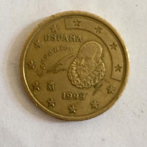 May include: A gold-coloured Spanish 1 cent euro coin featuring a portrait of Cervantes and the text "ESPAÑA" and "1999".