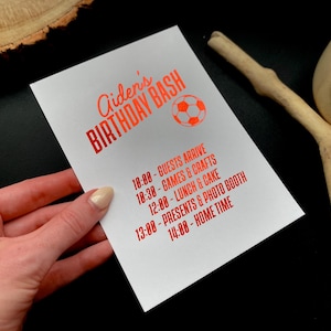 May include: White invitation card with red text that reads "Aiden's BIRTHDAY BASH" and a soccer ball graphic. The card lists the party schedule: Guests arrive at 10:00, Games & Crafts at 10:30, Lunch & Cake at 12:00, Presents & Photo Booth at 13:00, and Home Time at 14:00.